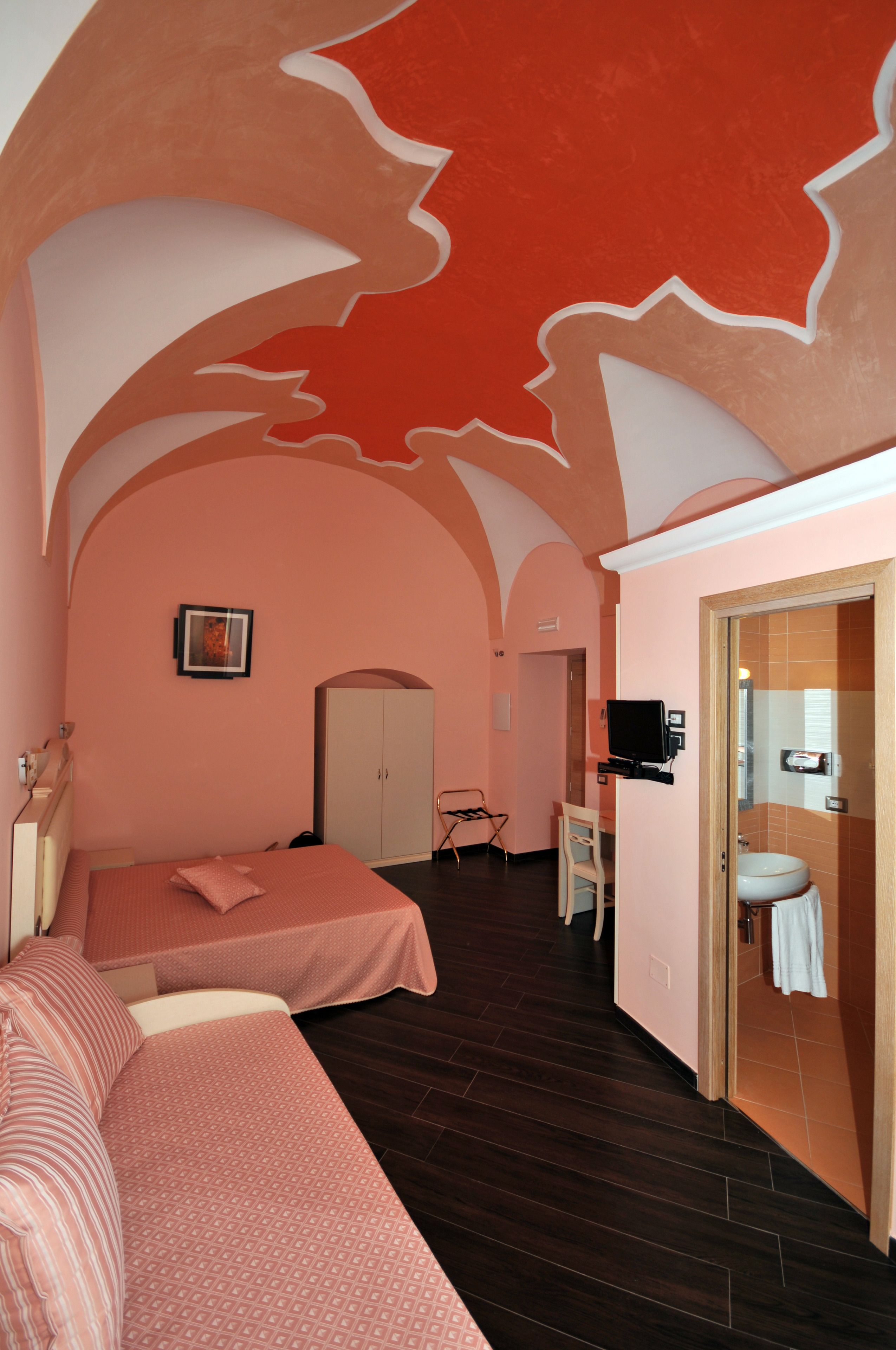 A bedroom with two beds, a television, a wardrobe, and a bathroom with a sink and mirror.