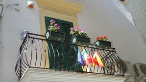 A balcony with metal railings, potted plants, and flags.
