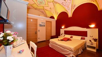 A bedroom with a bed, bedside tables, a desk with a laptop, and a red carpet.