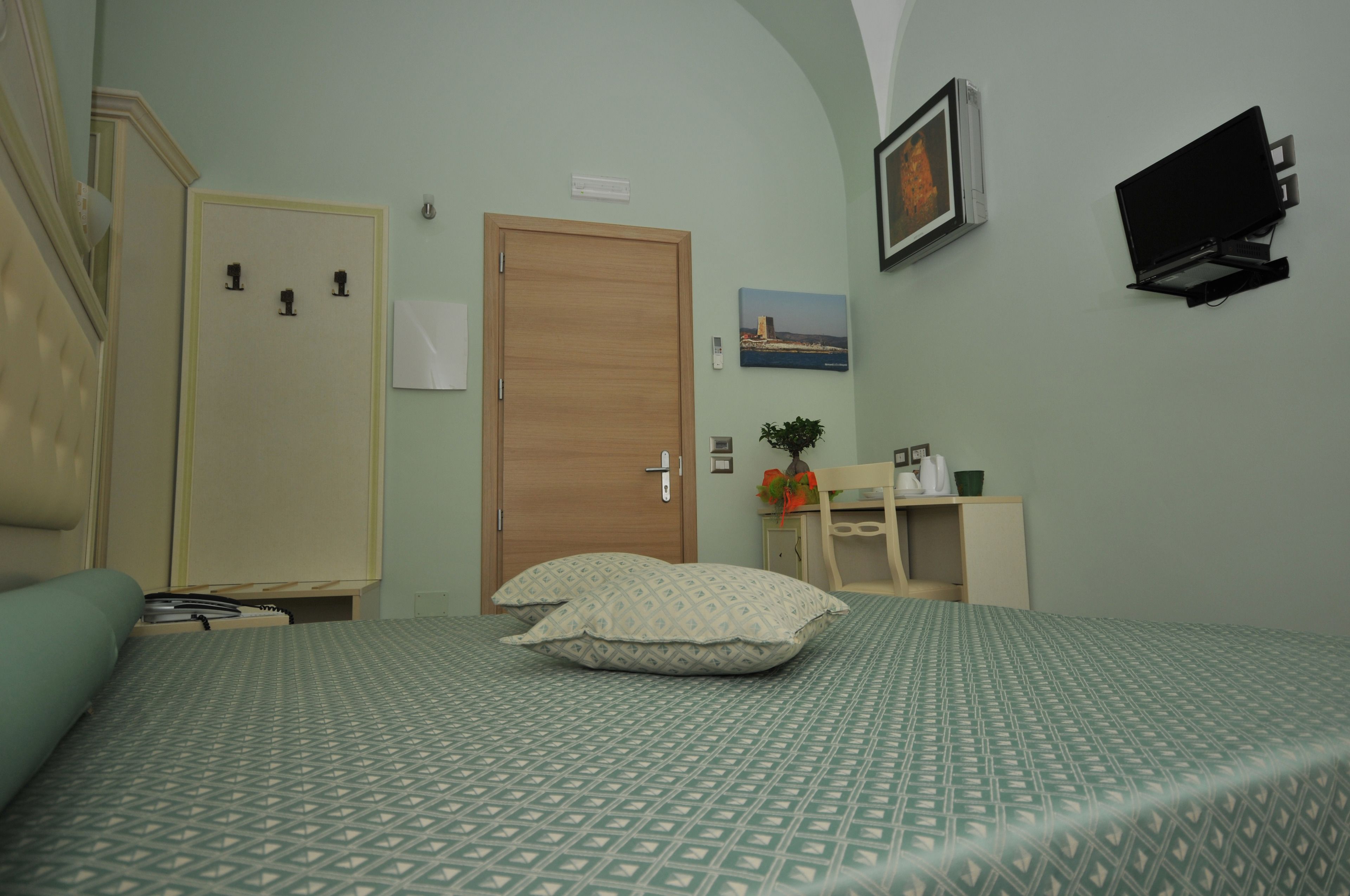 A hotel room with a bed, a desk, a chair, a TV, and a door.