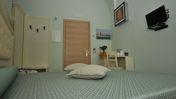 A hotel room with a bed, a desk, a chair, a TV, and a door.