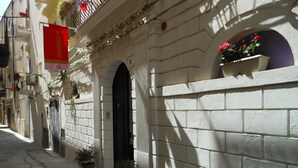 A narrow street with a building featuring a white brick facade, a black door, and a red banner.