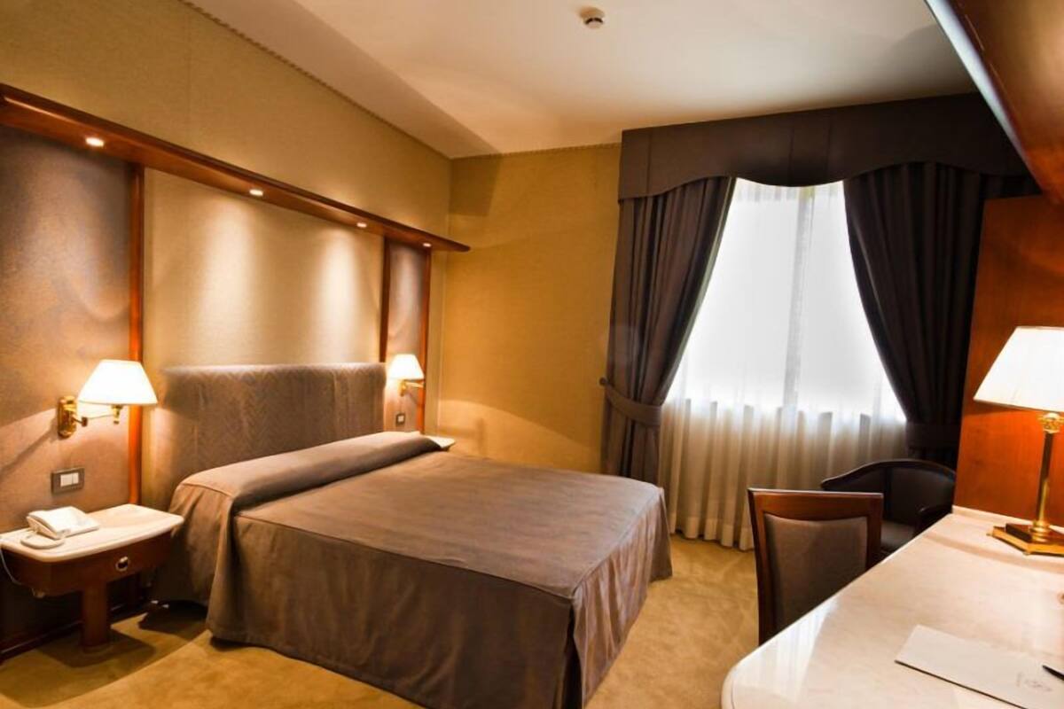 Ein Hotelzimmer mit einem Bett, zwei Nachttischen mit Lampen, einem Schreibtisch und einem Stuhl.