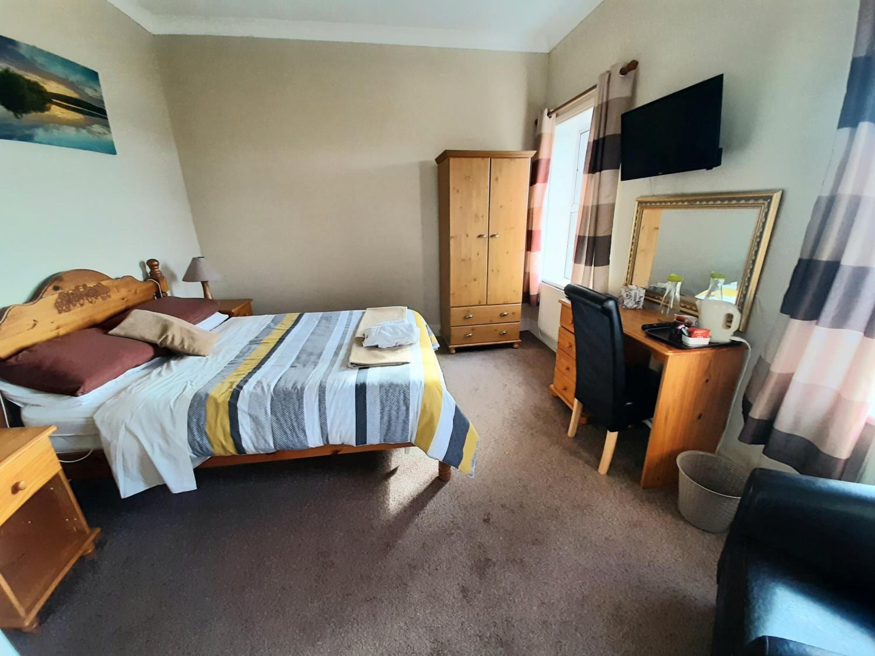A bedroom with a bed, wooden wardrobe, desk, chair, and a television mounted on the wall.