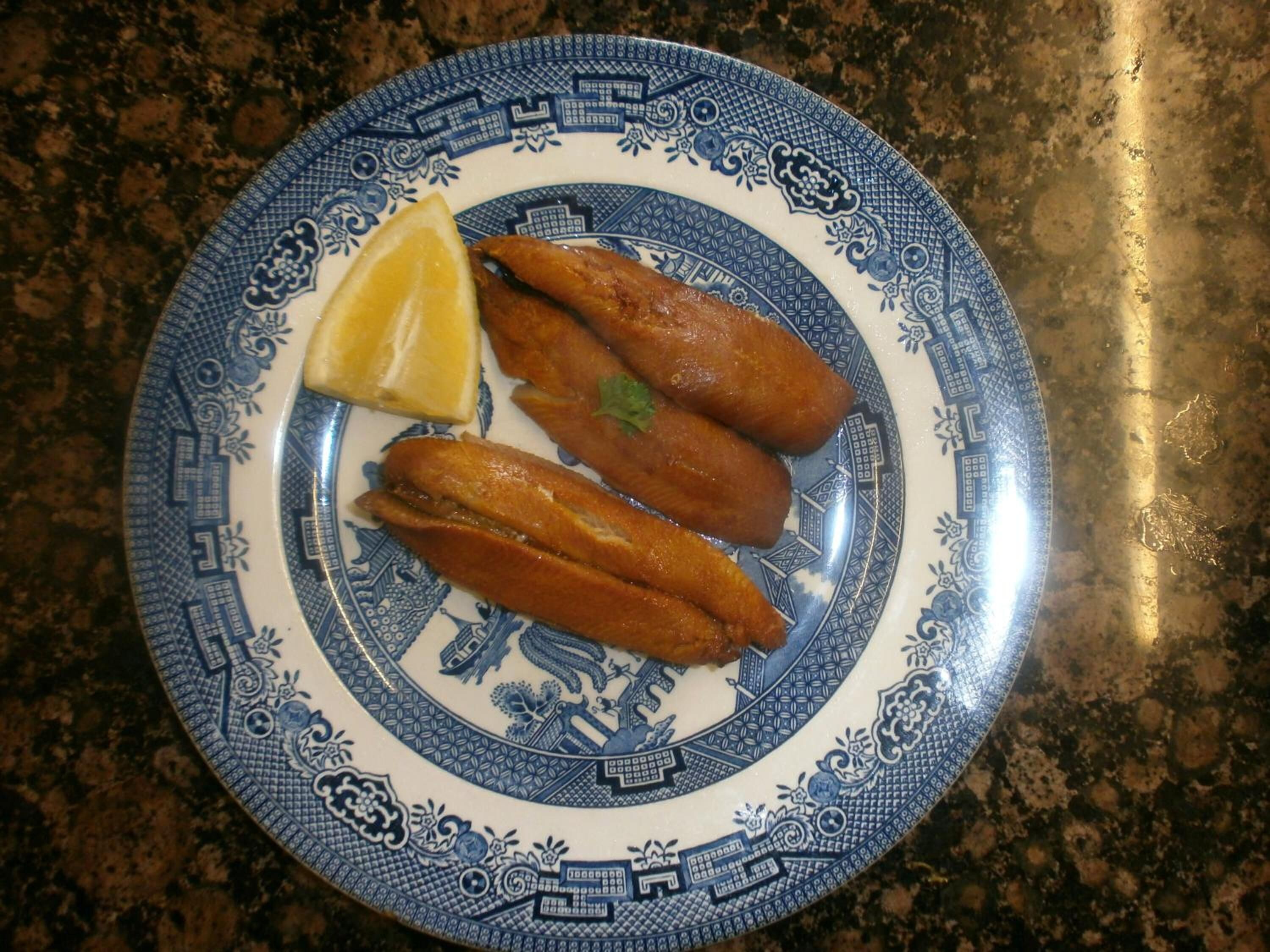 A plate with two pieces of fried fish and a lemon wedge on a blue and white patterned plate.