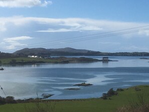 A tranquil lakeside view with a small house on the shore, surrounded by hills and a clear sky.
