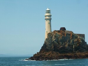 A lighthouse on a rocky outcrop with the sea in the foreground.