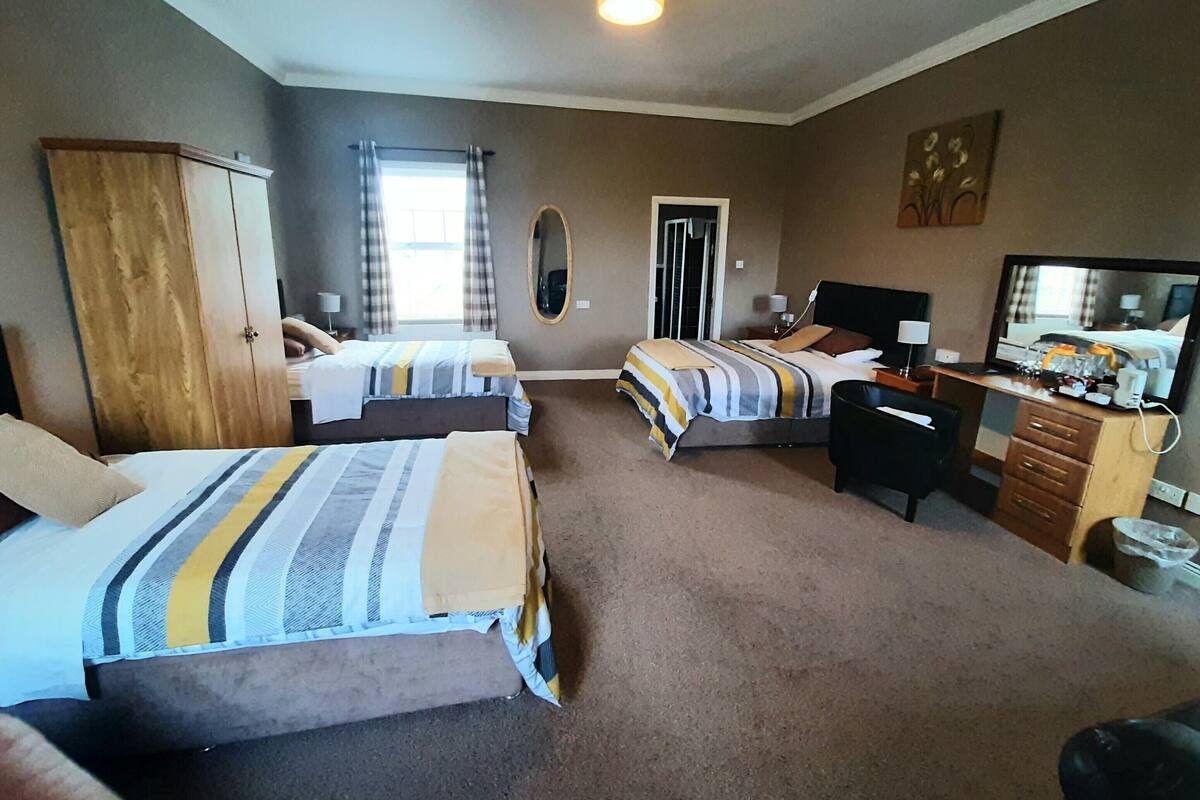 A hotel room with two beds, a desk, a chair, a wardrobe, a television, and a door leading to a balcony.