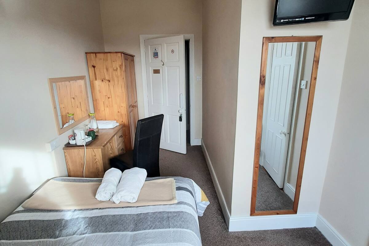 A hotel room with a bed, a wooden dresser, a mirror, a television, and a door.