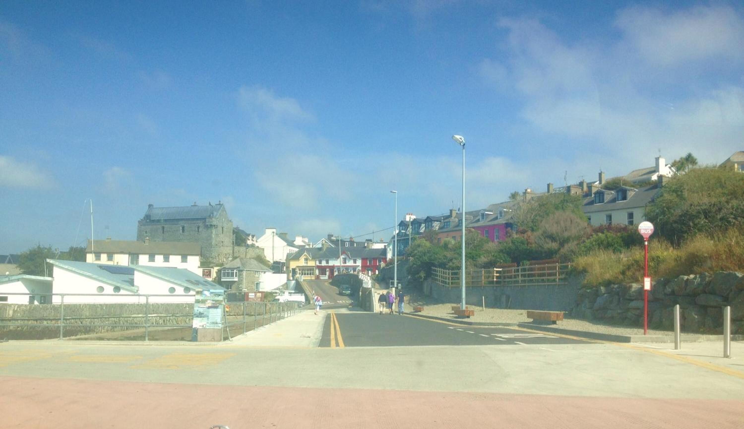 A coastal town with a prominent castle-like building, a pedestrian bridge, and a bus stop.