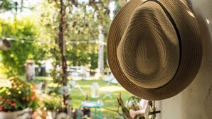 Un barret de palla penjat a la paret, amb un jardí i una zona d'estar a l'aire lliure al fons.