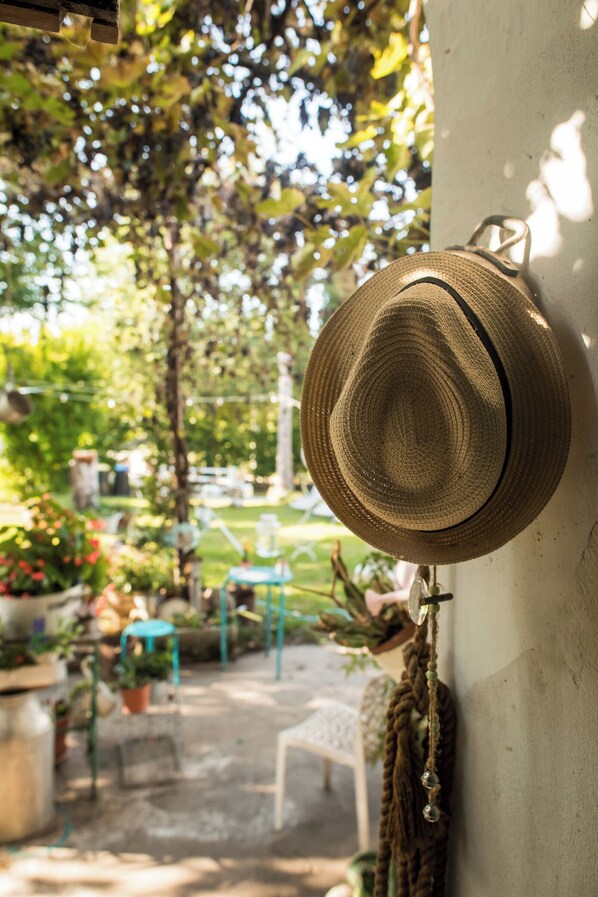 Un sombrero de paja colgado en una pared, con un jardín y una zona de estar al aire libre al fondo.