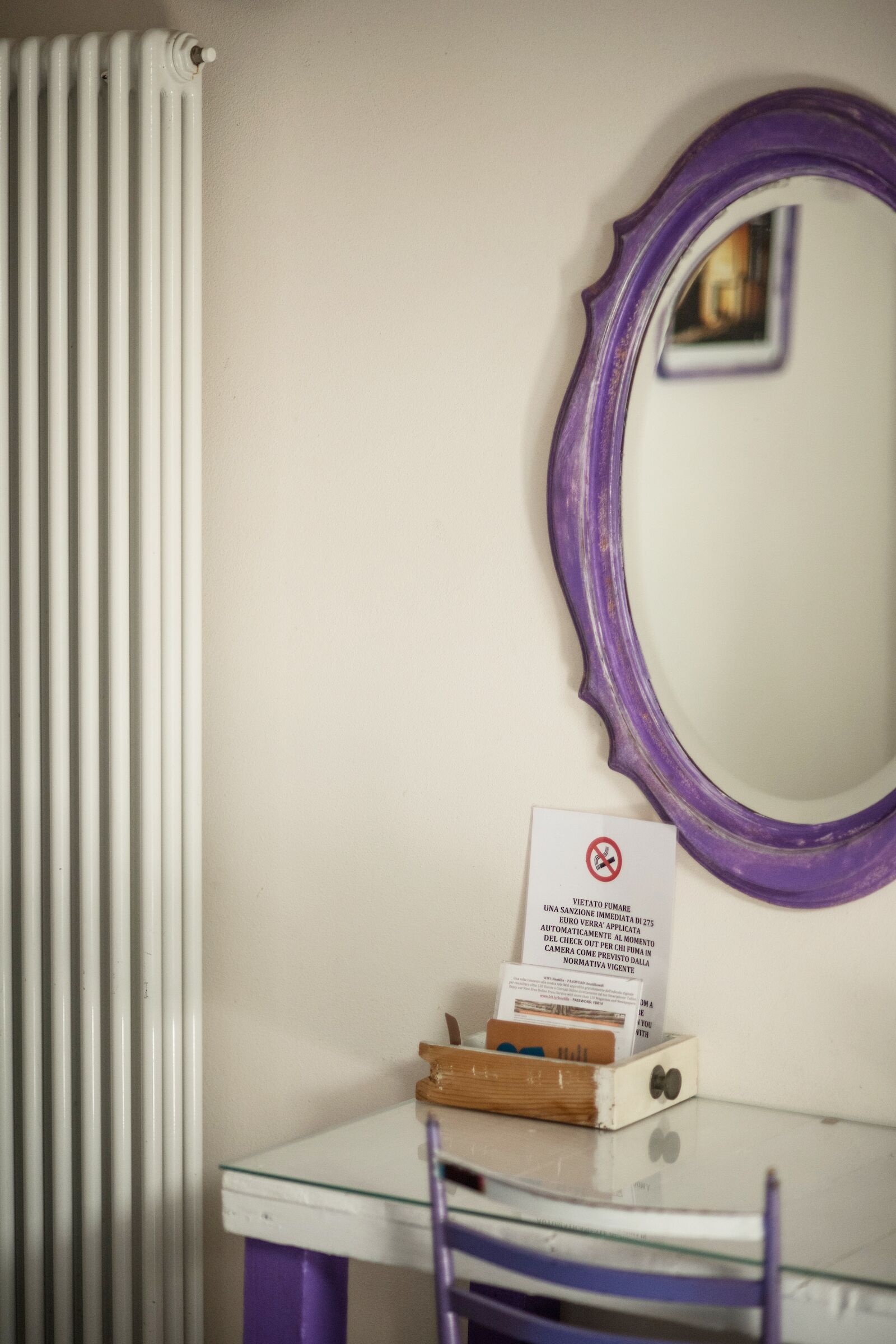 Ein Zimmer mit Heizkörper, Spiegel mit violetter Rahmen und Tisch mit einem Schild.