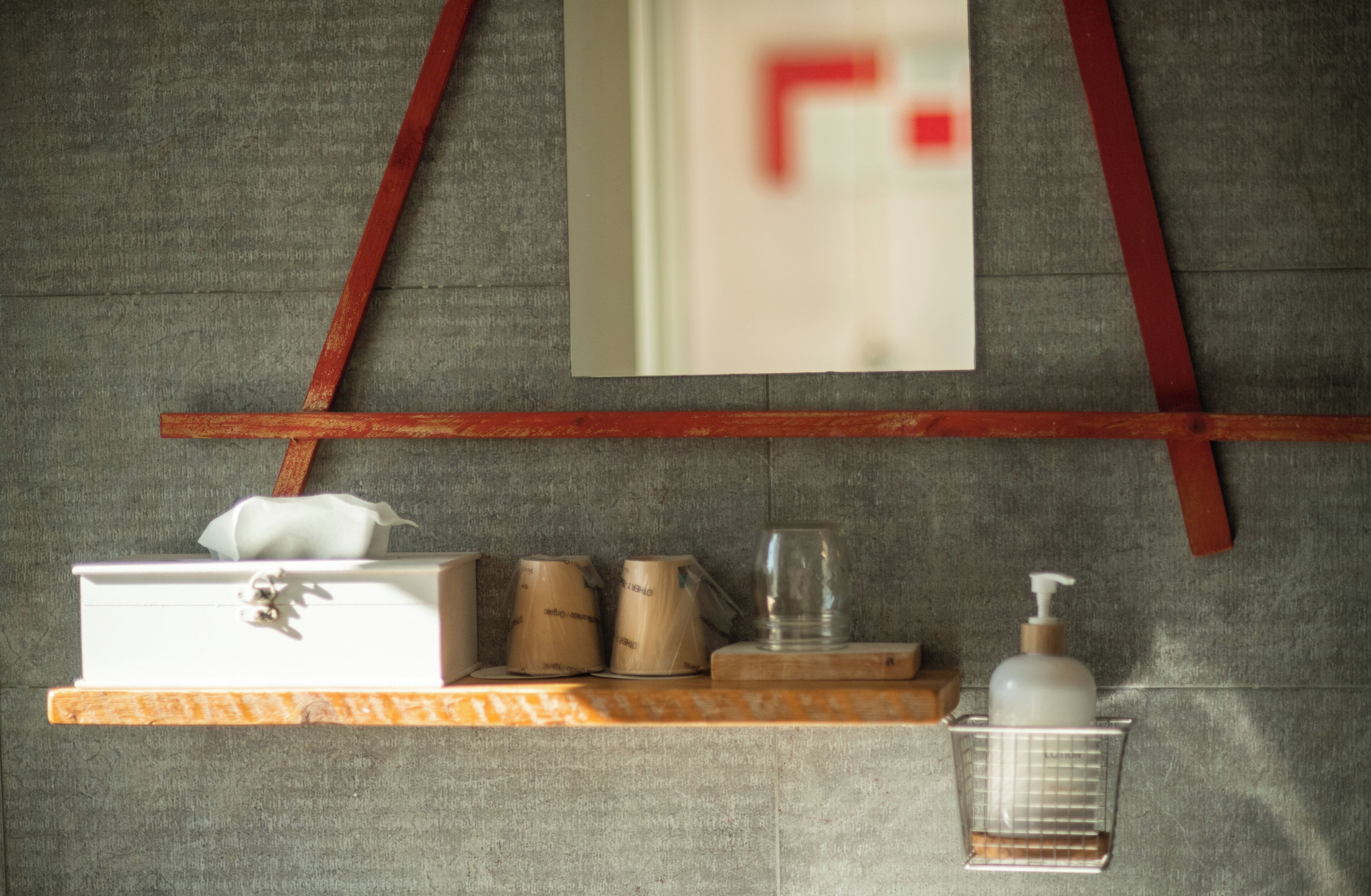 A bathroom with a mirror, a shelf with toiletries, and a red-framed window.