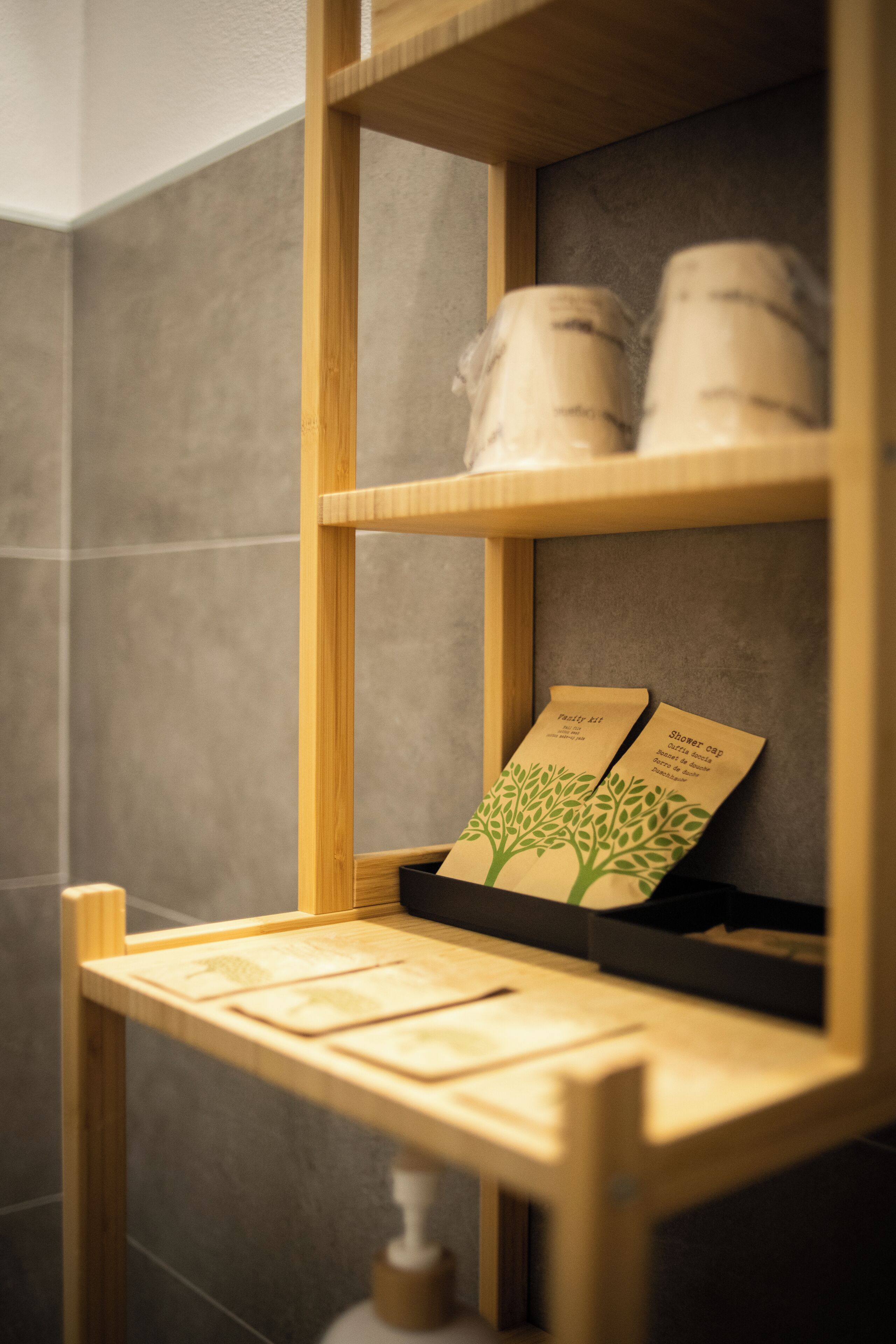 A wooden shelf with two items labeled 'Shower cap' and 'Facial kit' against a tiled wall.