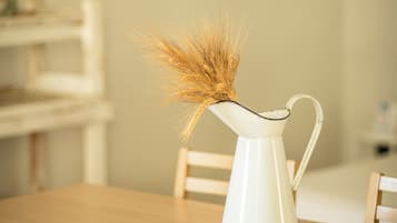 Een witte karaf met korenaren op een houten tafel, omringd door houten stoelen.