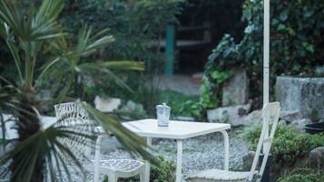 Eine Terrasse im Freien mit einem weißen Tisch und Stuhl unter einem weißen Sonnenschirm, umgeben von Kübelpflanzen und Kies.
