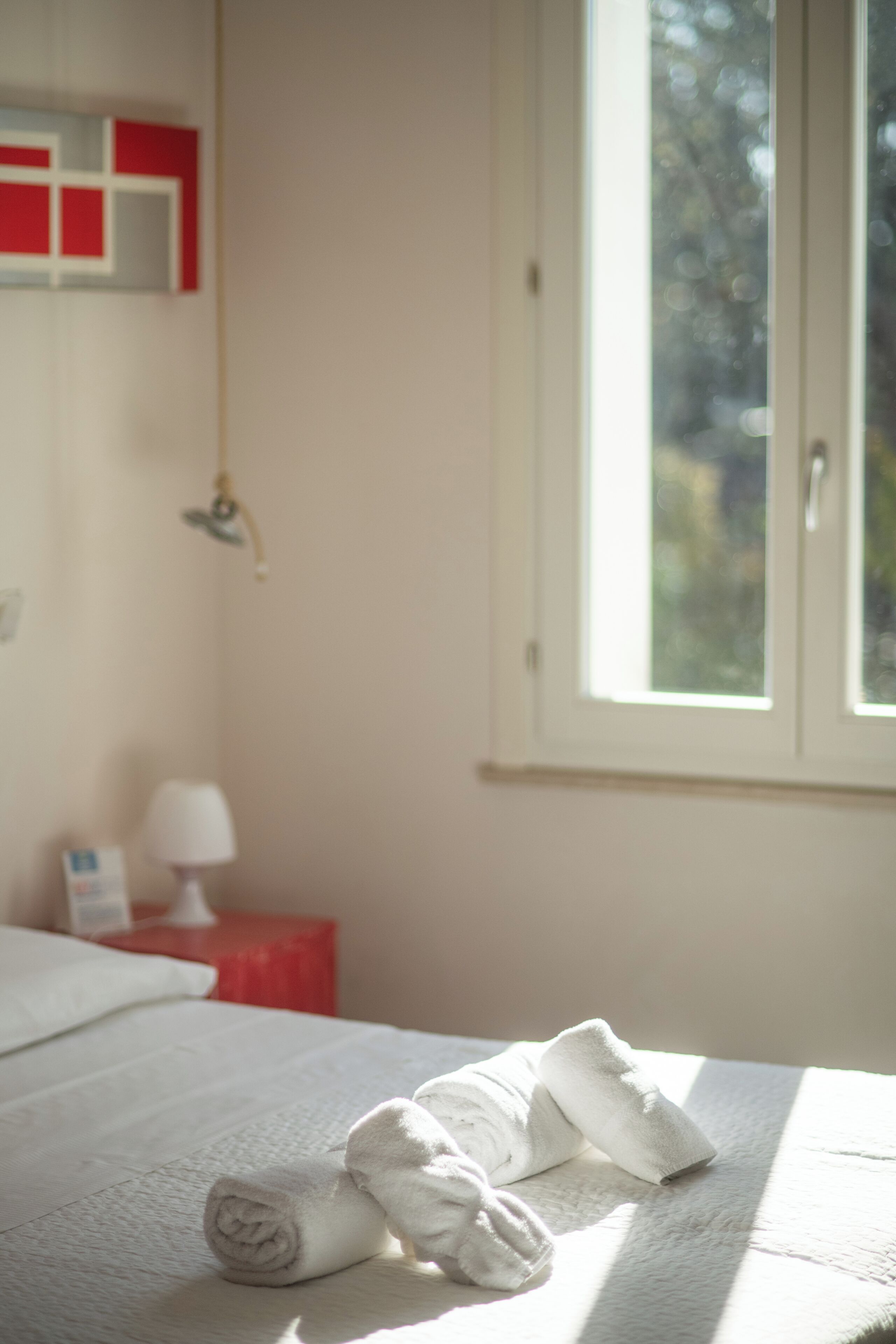 Een hotelkamer met een bed, een raam en een nachtkastje in het rood met een lamp.