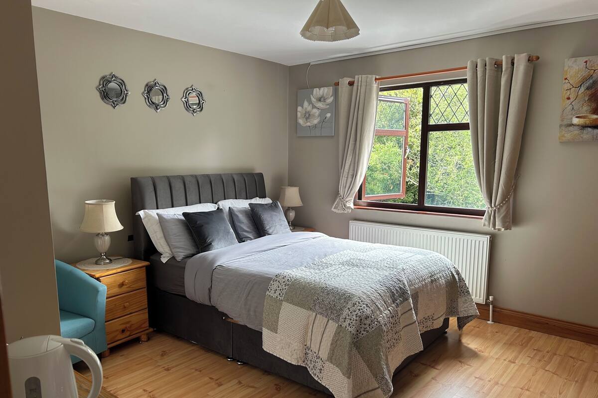 A bedroom with a bed, bedside table, lamp, and a window with curtains.