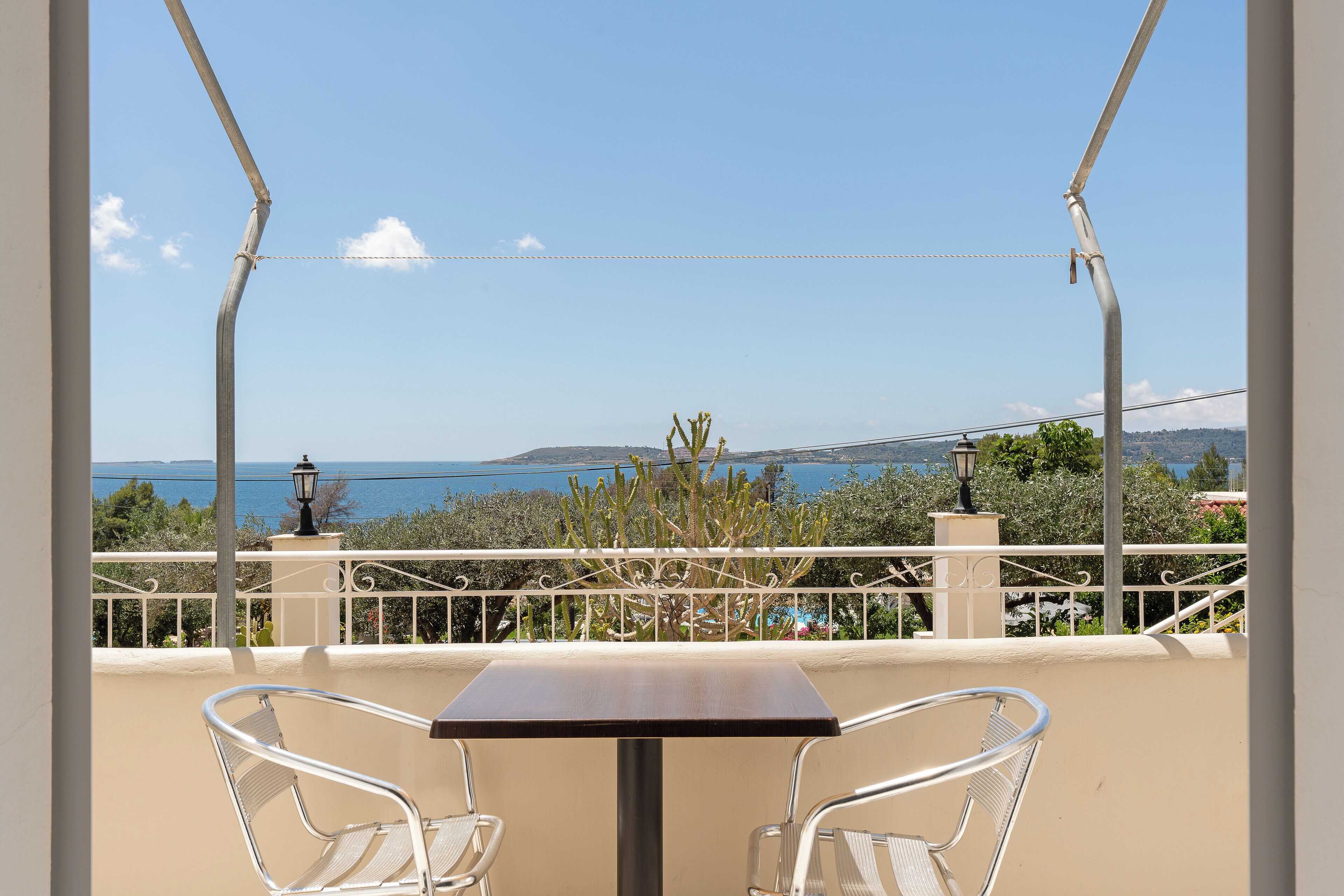 Un balcon avec deux chaises en métal et une table, offrant une vue panoramique sur la mer et les collines.