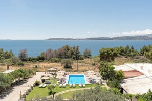 A pool area with a view of the sea, surrounded by greenery and a few buildings. - Oskars Studios & Apartments (Kefalonia)