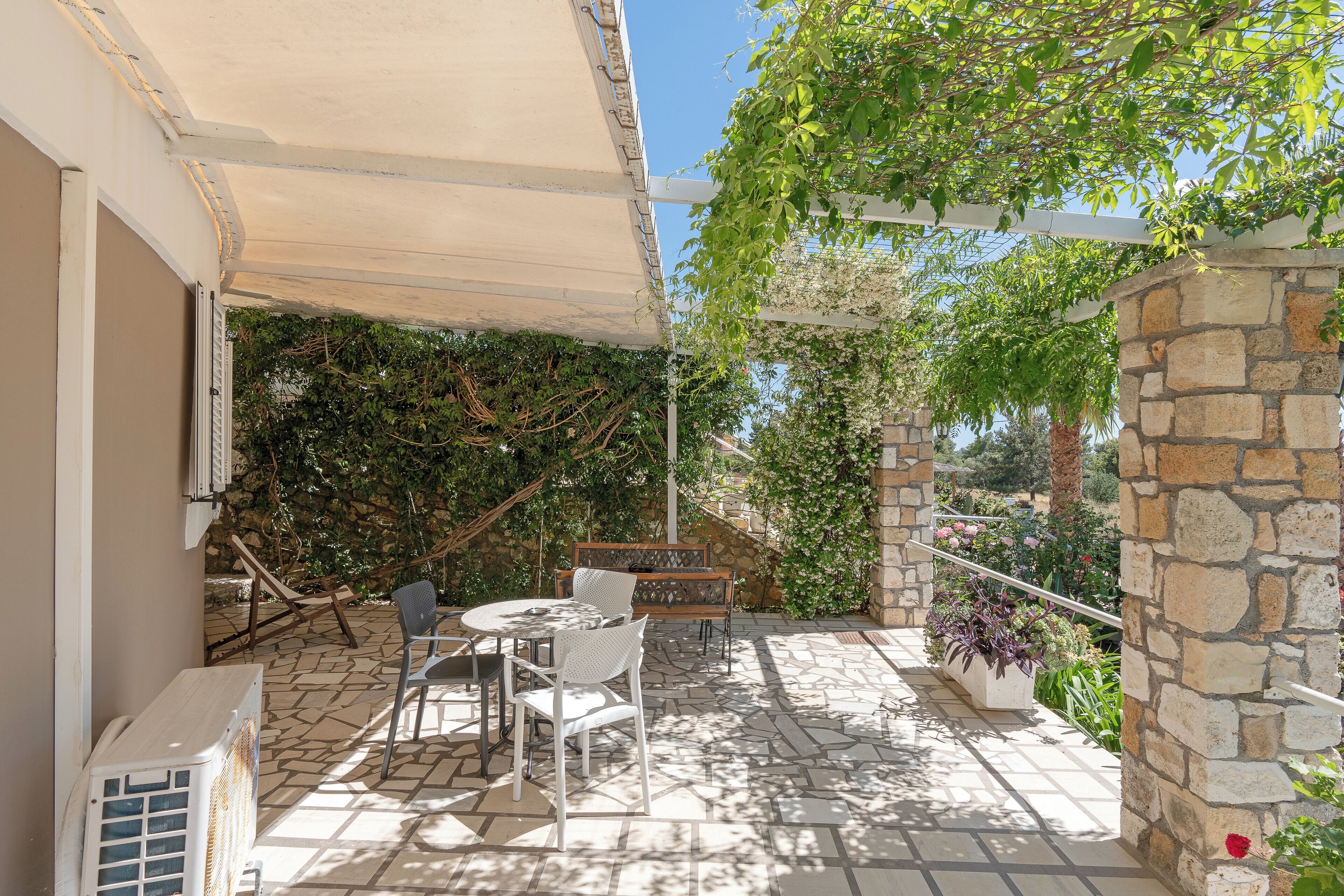 Un patio con mesa y sillas, un muro de piedra y una pérgola con plantas trepadoras.