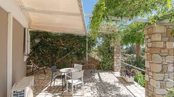 A patio with a table and chairs, a stone wall, and a pergola with climbing plants.