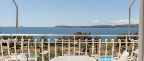 A balcony with a table and chairs, a pool, and a view of the sea.