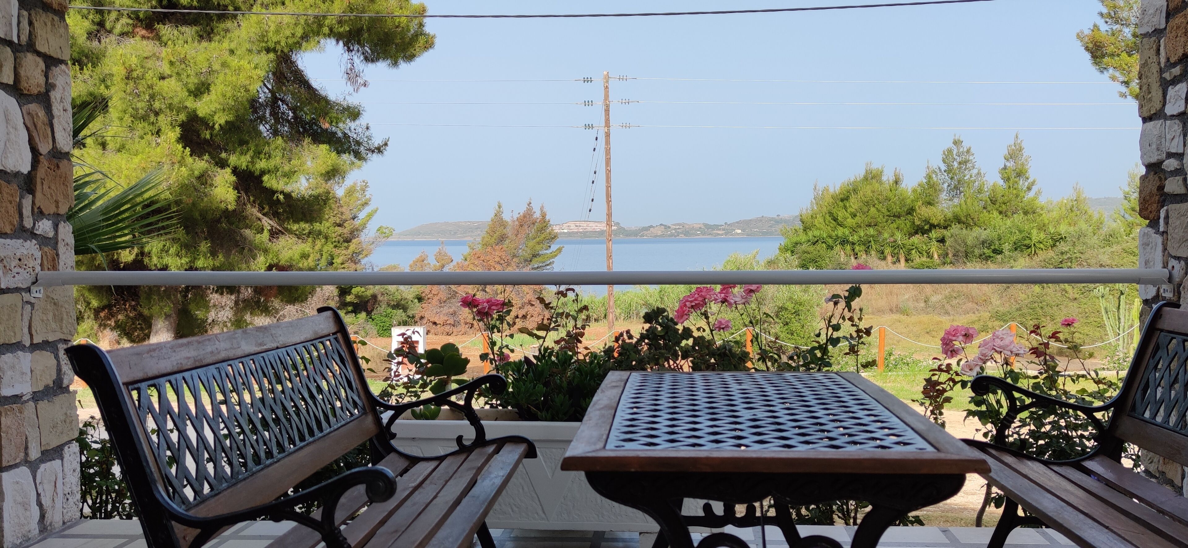Un balcón con una mesa y dos bancos, con vista a una masa de agua y follaje.