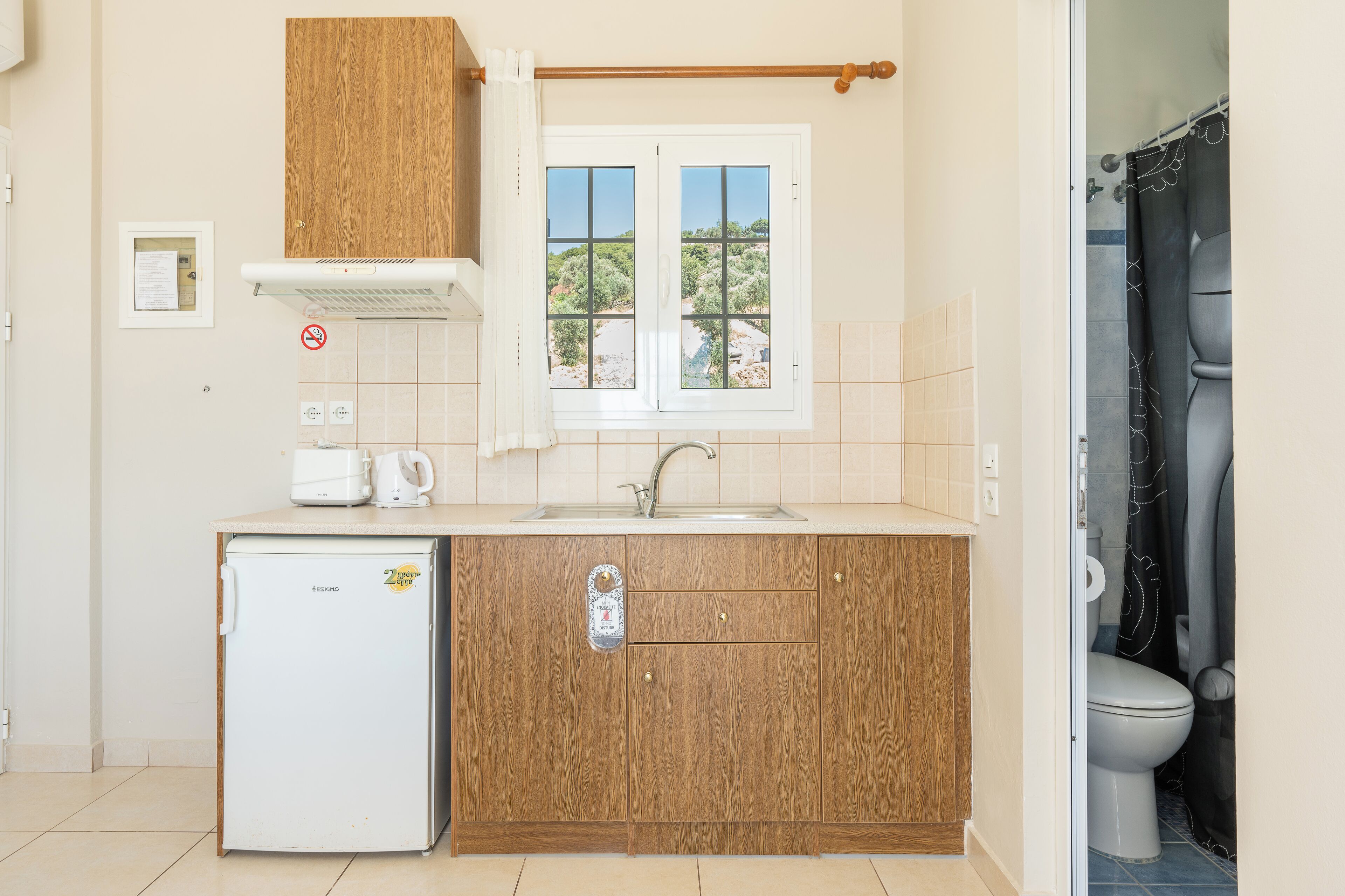 Cocina compacta con refrigerador, lavamanos y armarios de madera.