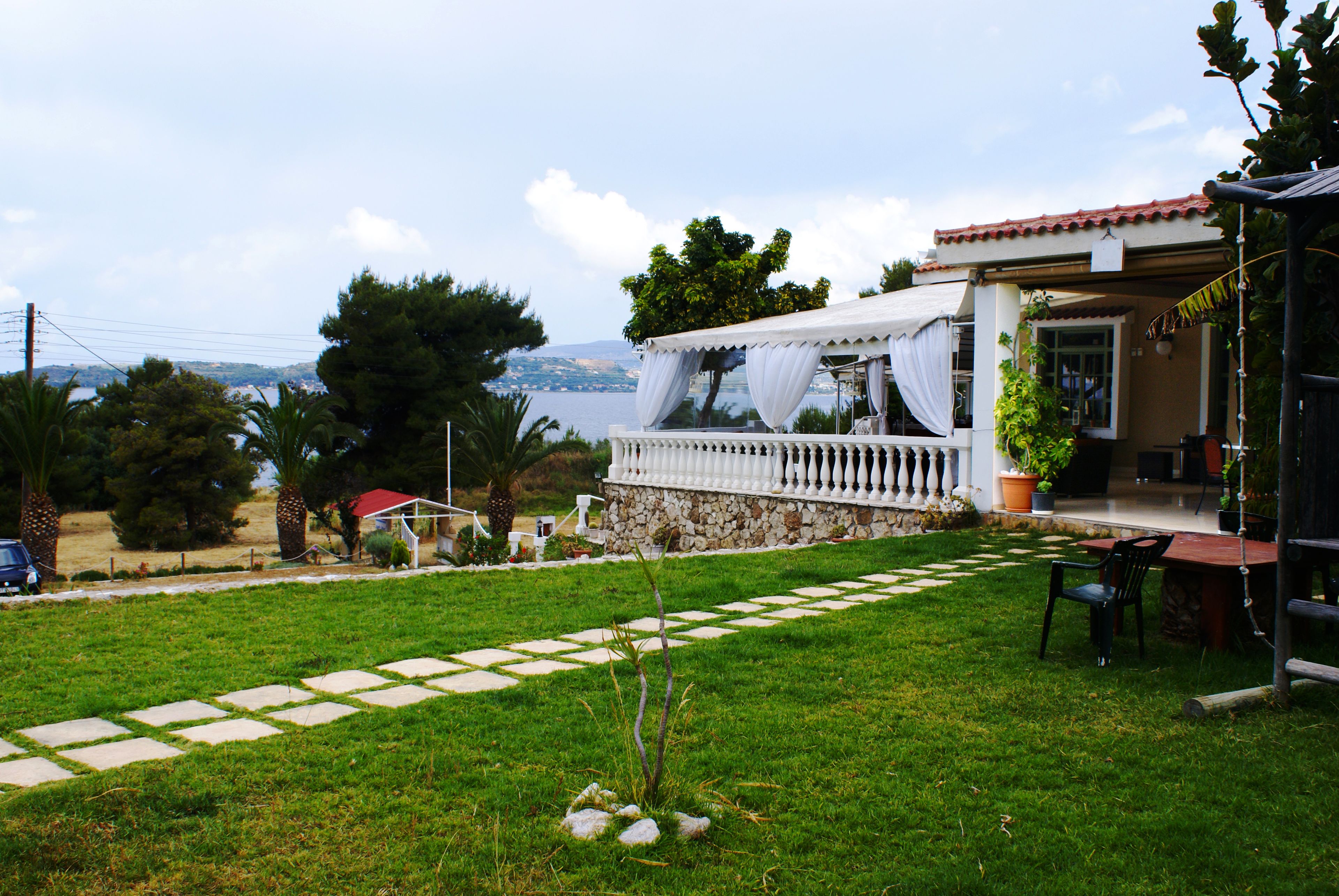 A house with a balcony overlooking a body of water, a stone wall, and a garden with a stone pathway.