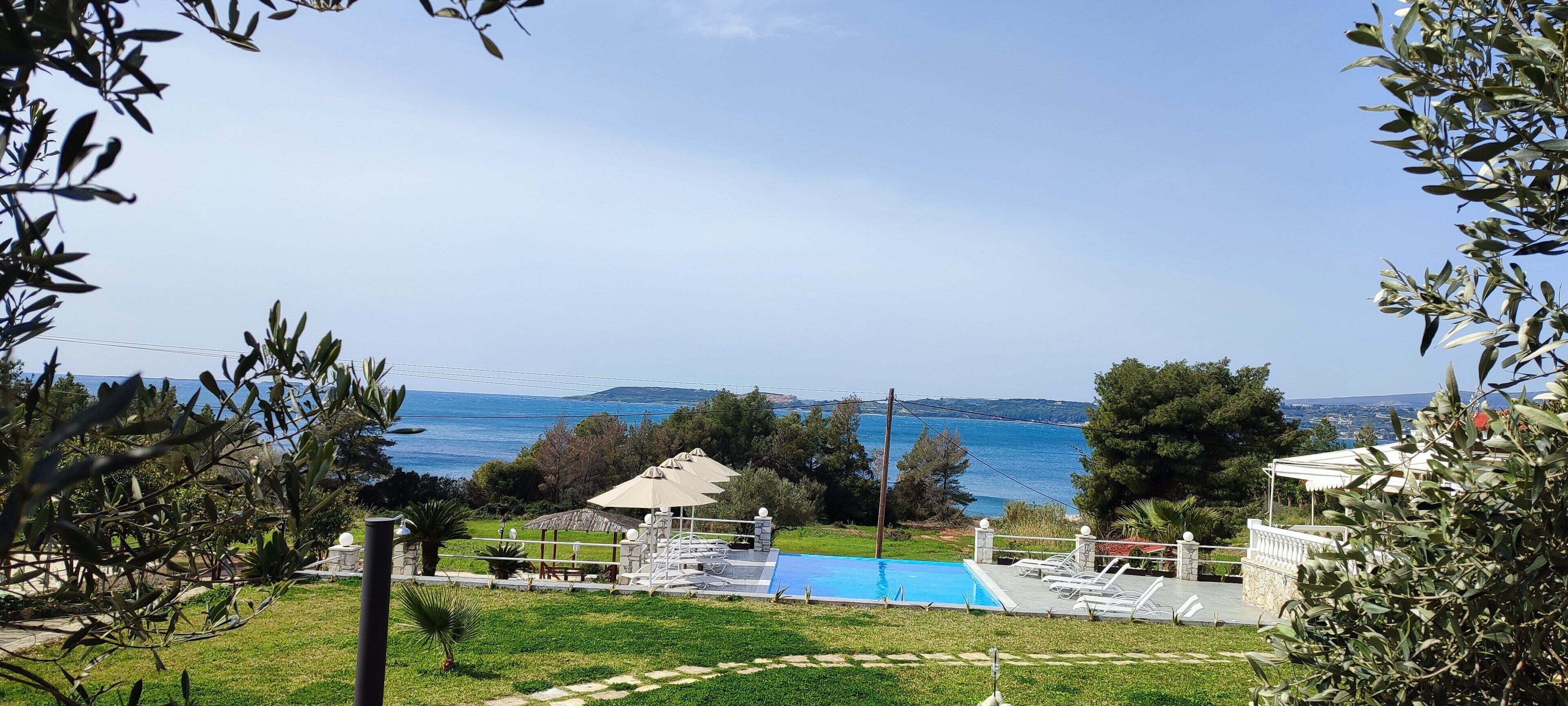 Vista de una piscina con sillones de descanso, un pabellón y vista al mar.