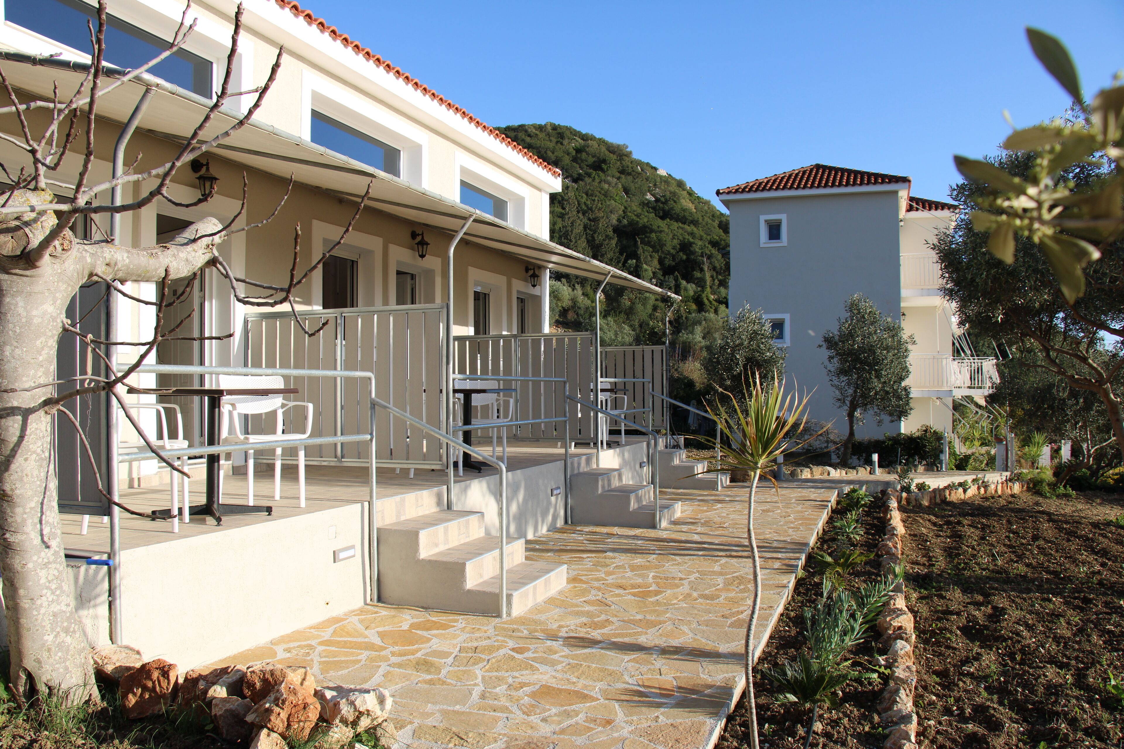 A modern building with a stone pathway leading to a covered outdoor seating area with tables and chairs.