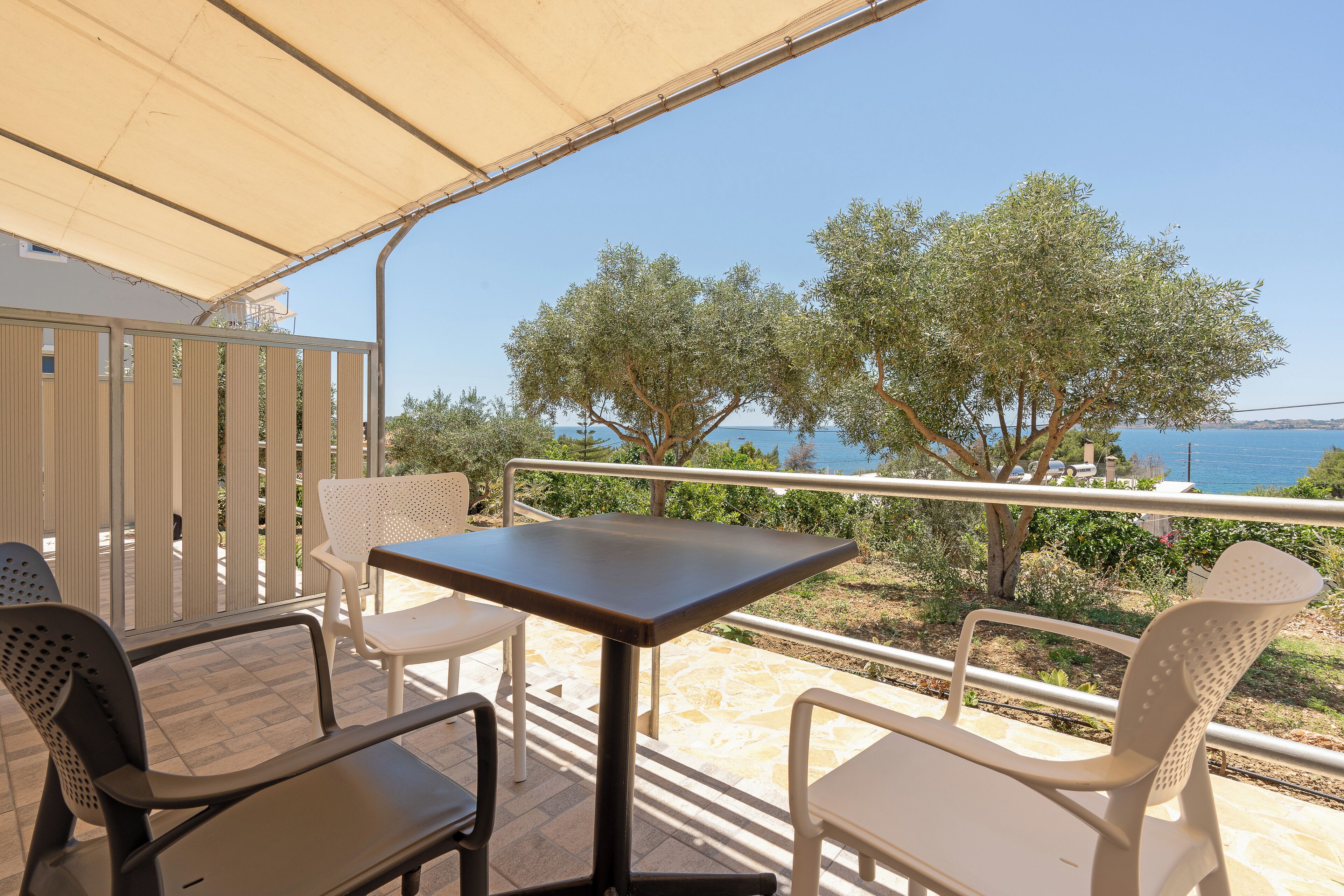 An outdoor seating area with a table and chairs, overlooking a body of water and trees.