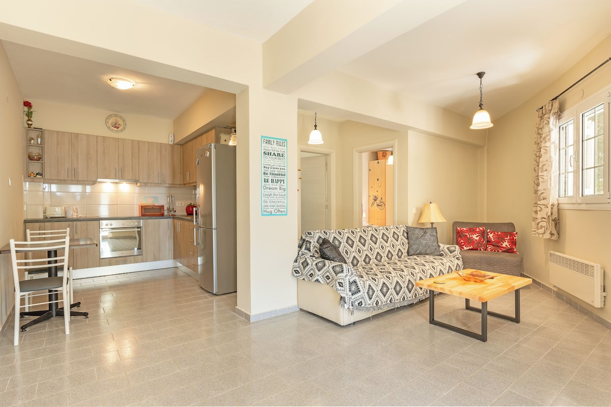 A modern apartment with a kitchen, dining area, and living room. It features a dining table, a sofa, and a coffee table.