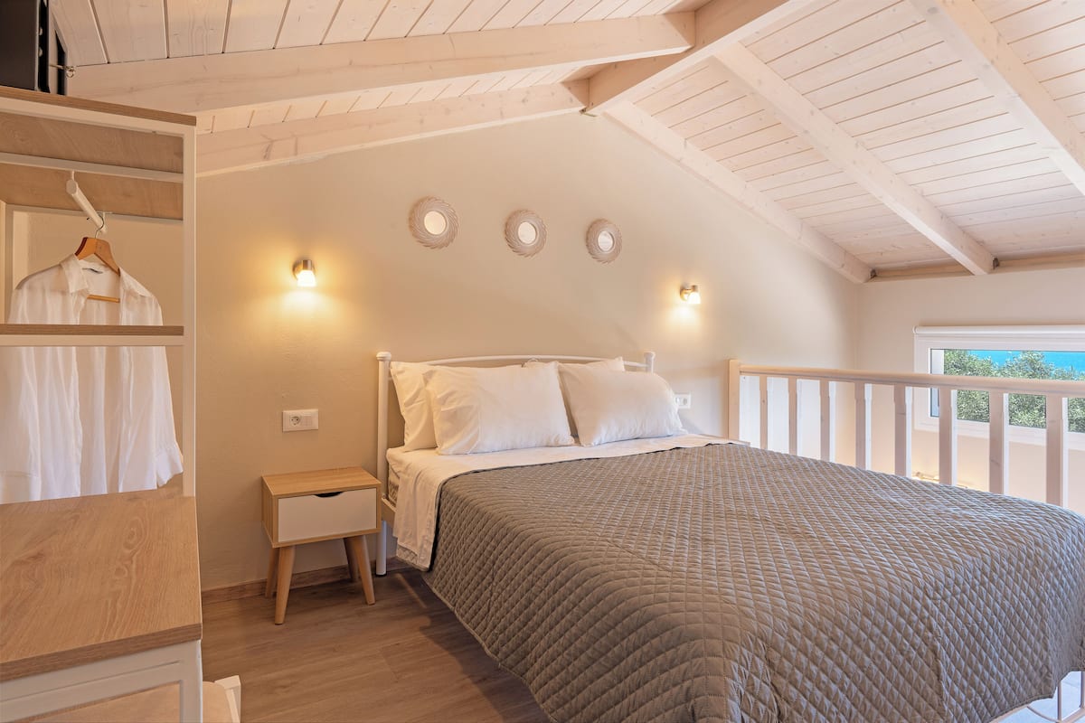 A bedroom with a wooden ceiling, a bed with white bedding, a bedside table, and a wardrobe.