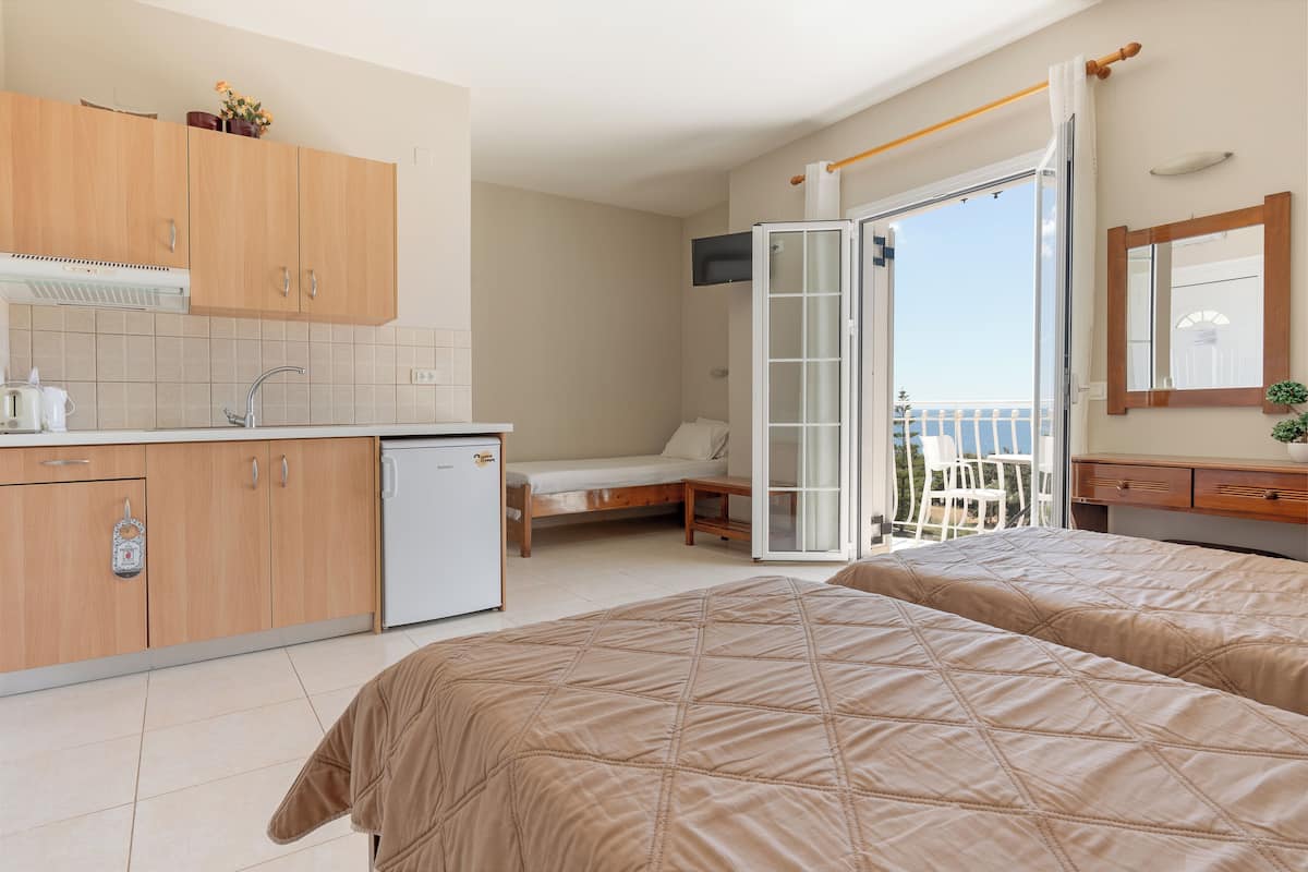 A hotel room with a kitchenette, a bed, a balcony with a view, and a bathroom.
