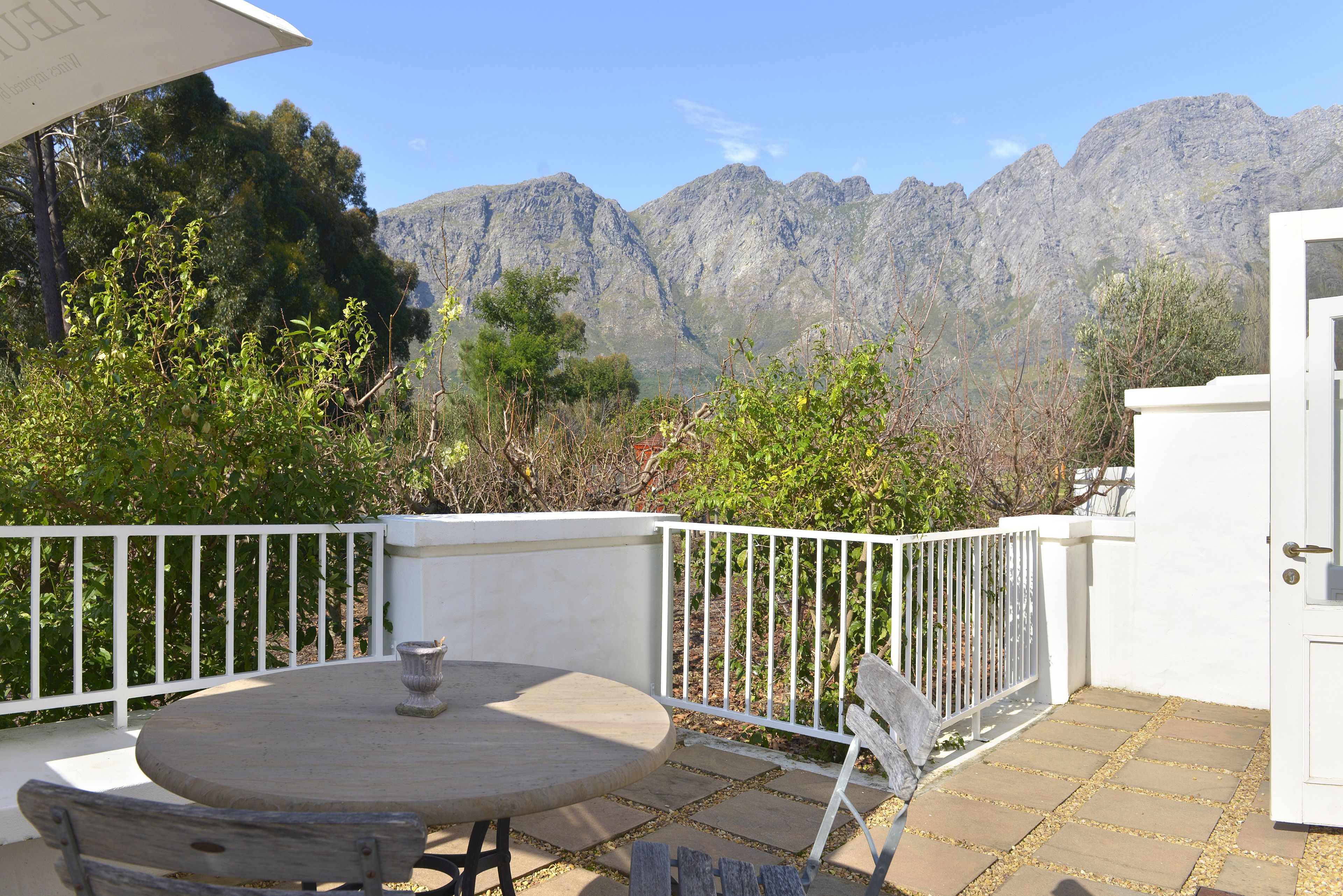 A patio with a round table and benches, white railing, and a view of mountains.