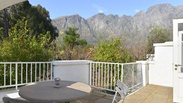 A patio with a round table and benches, white railing, and a view of mountains.