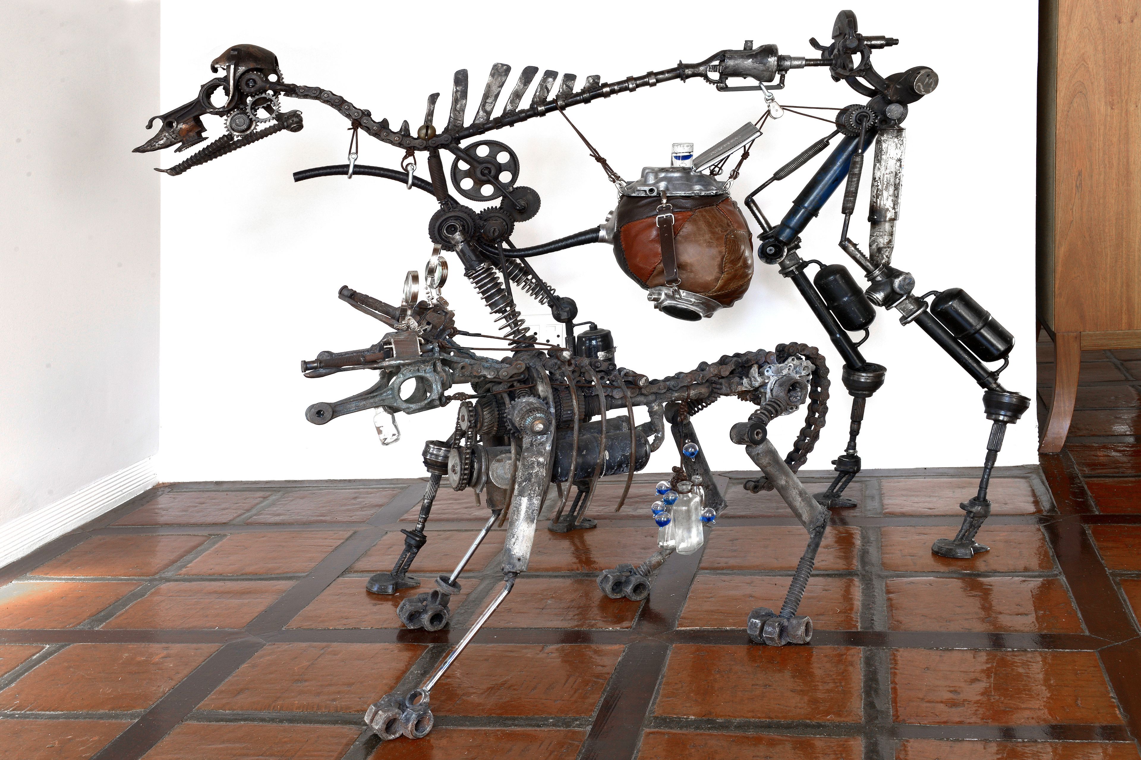 A sculpture resembling a mechanical creature with a pot on its back, set against a white wall on a tiled floor.