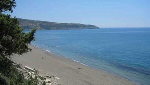 Ein Strand mit klarem, blauem Wasser, einem sandigen Ufer und einer entfernten Hügelkette.