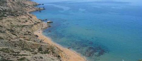 Un paisaje costero con una playa, acantilados y un pequeño edificio.