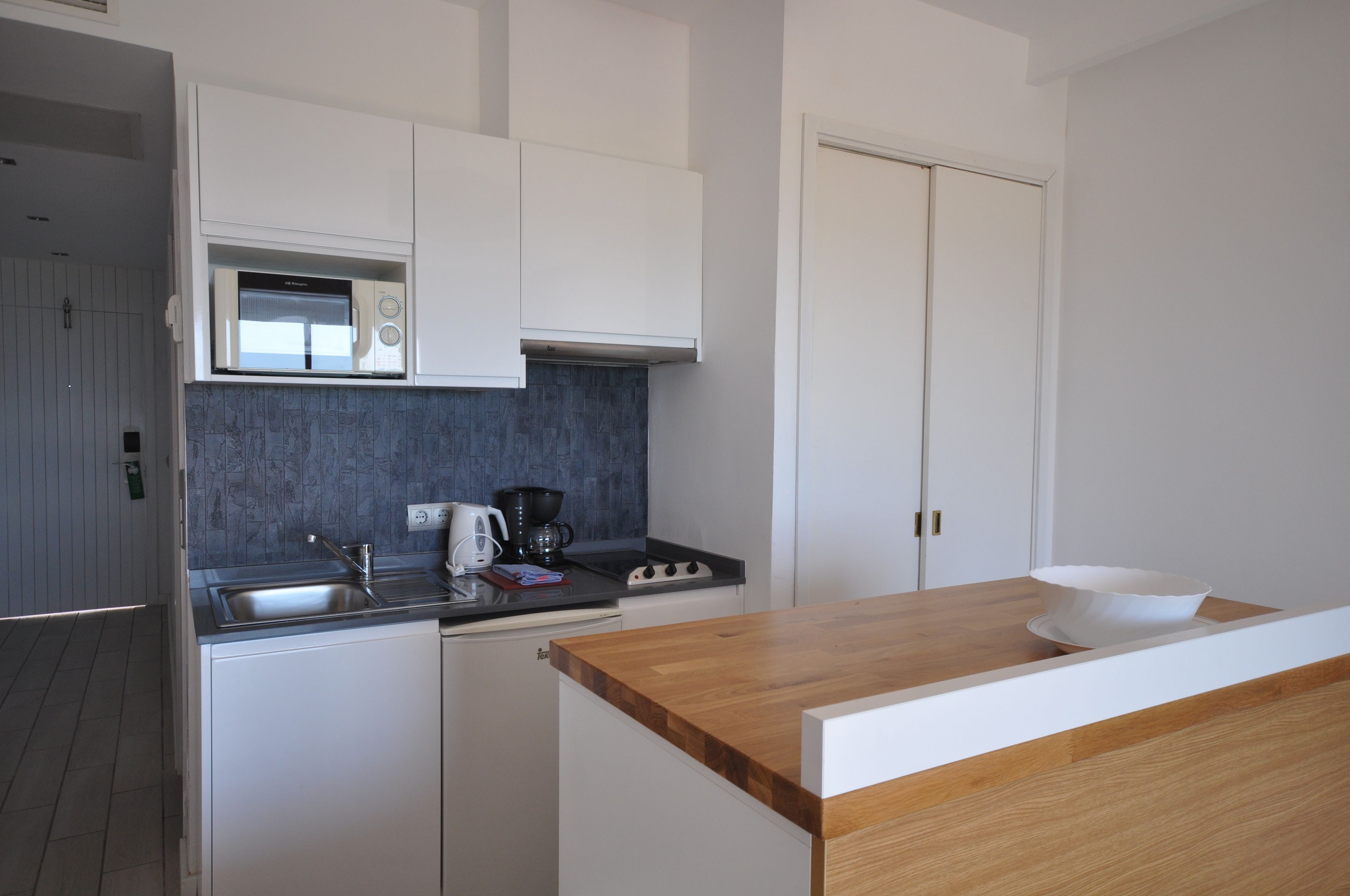 Une cuisine moderne avec des meubles blancs, un four à micro-ondes, une machine à café et un plan de travail en bois.