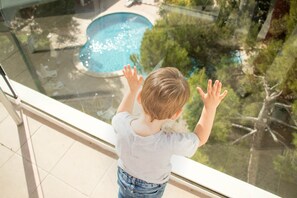 Un enfant regarde par-dessus le bord d’un balcon, avec une piscine en arrière-plan.