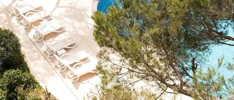 A pool area with white lounge chairs and a tree in the background.