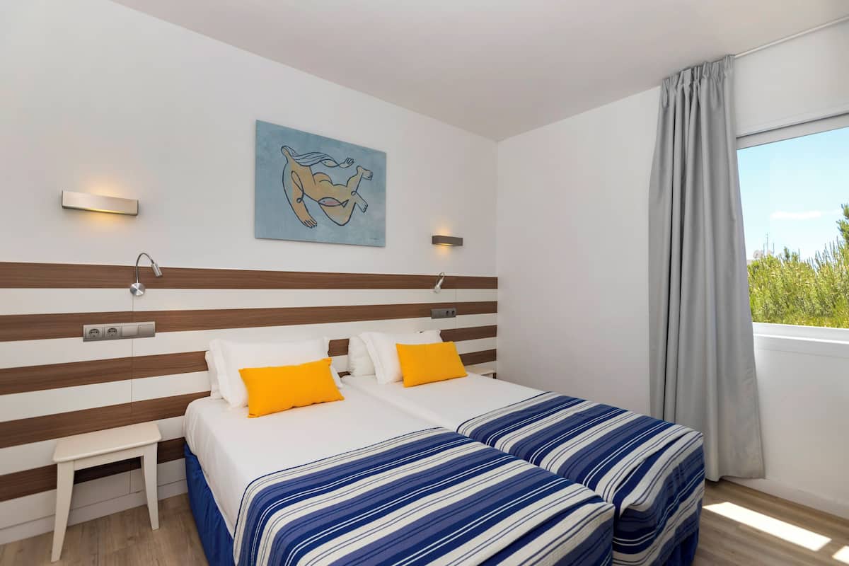 Een hotelkamer met een gestreept hoofdeinde, twee bedden met blauw-wit gestreept beddengoed, een klein wit nachtkastje en een schilderij aan de muur.