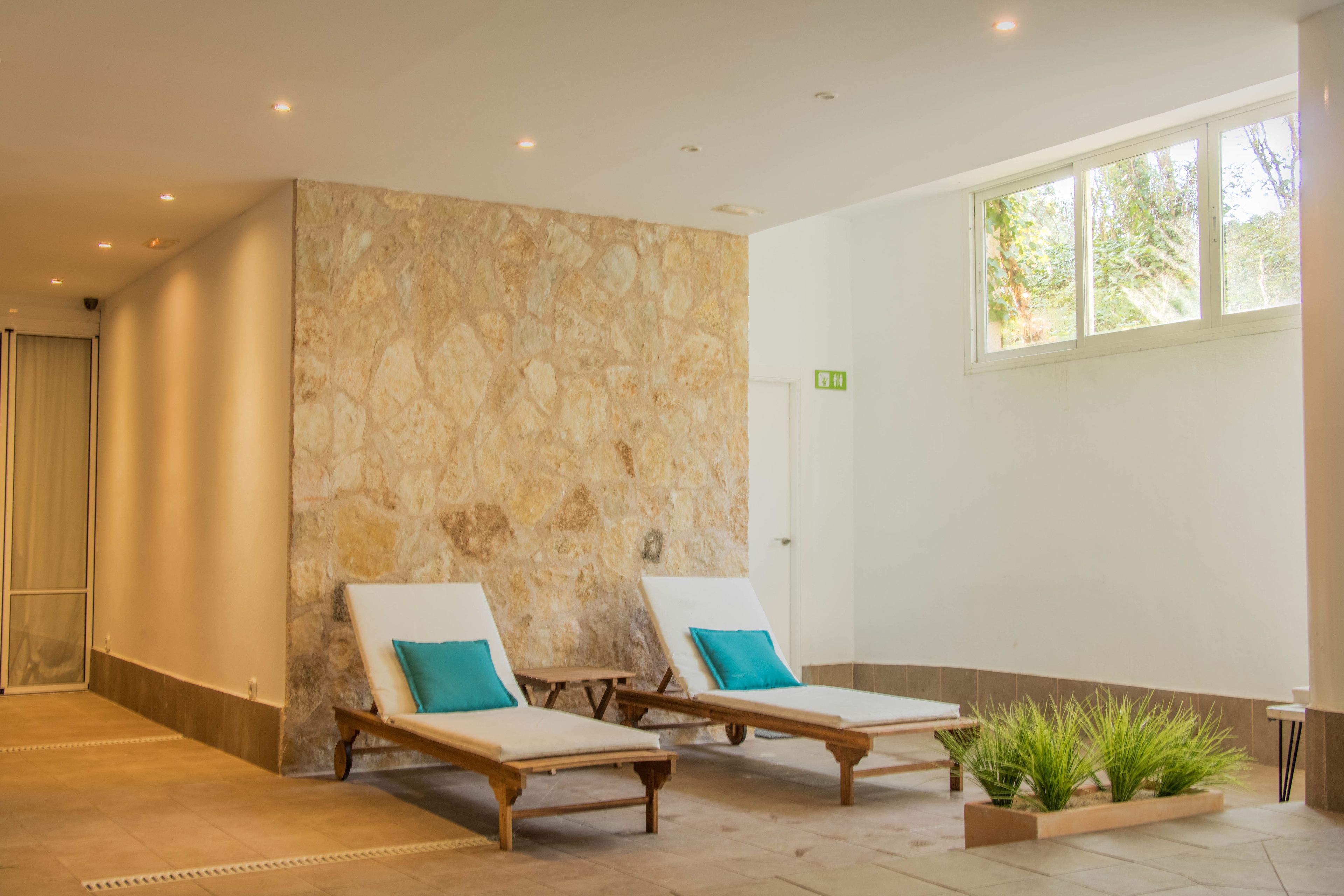 Zona de spa con dos tumbonas, una pared de piedra y una ventana con vistas a la vegetación.
