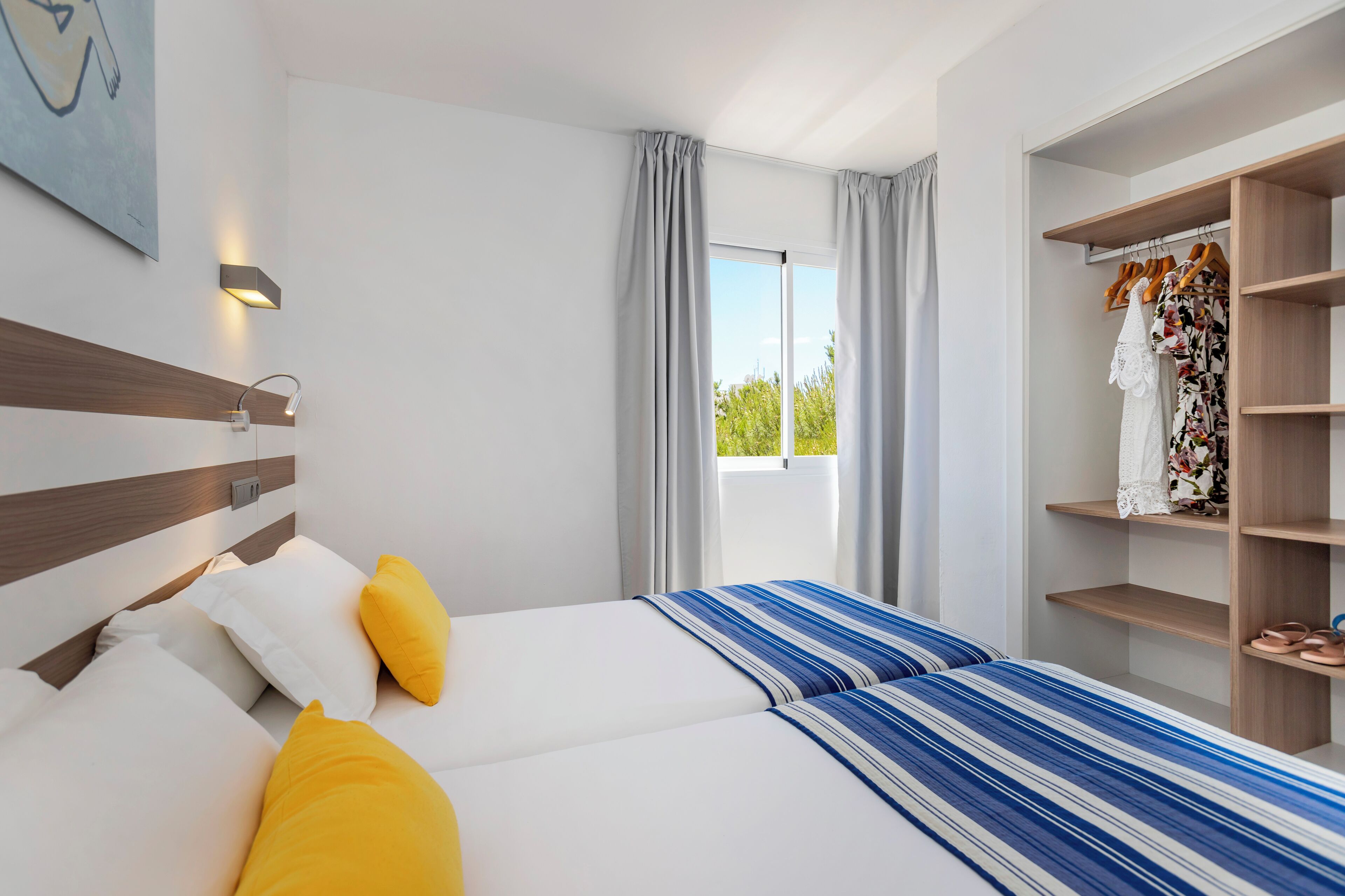 Une chambre d’hôtel avec deux lits, une armoire, une fenêtre avec des rideaux et un luminaire fixé au mur.