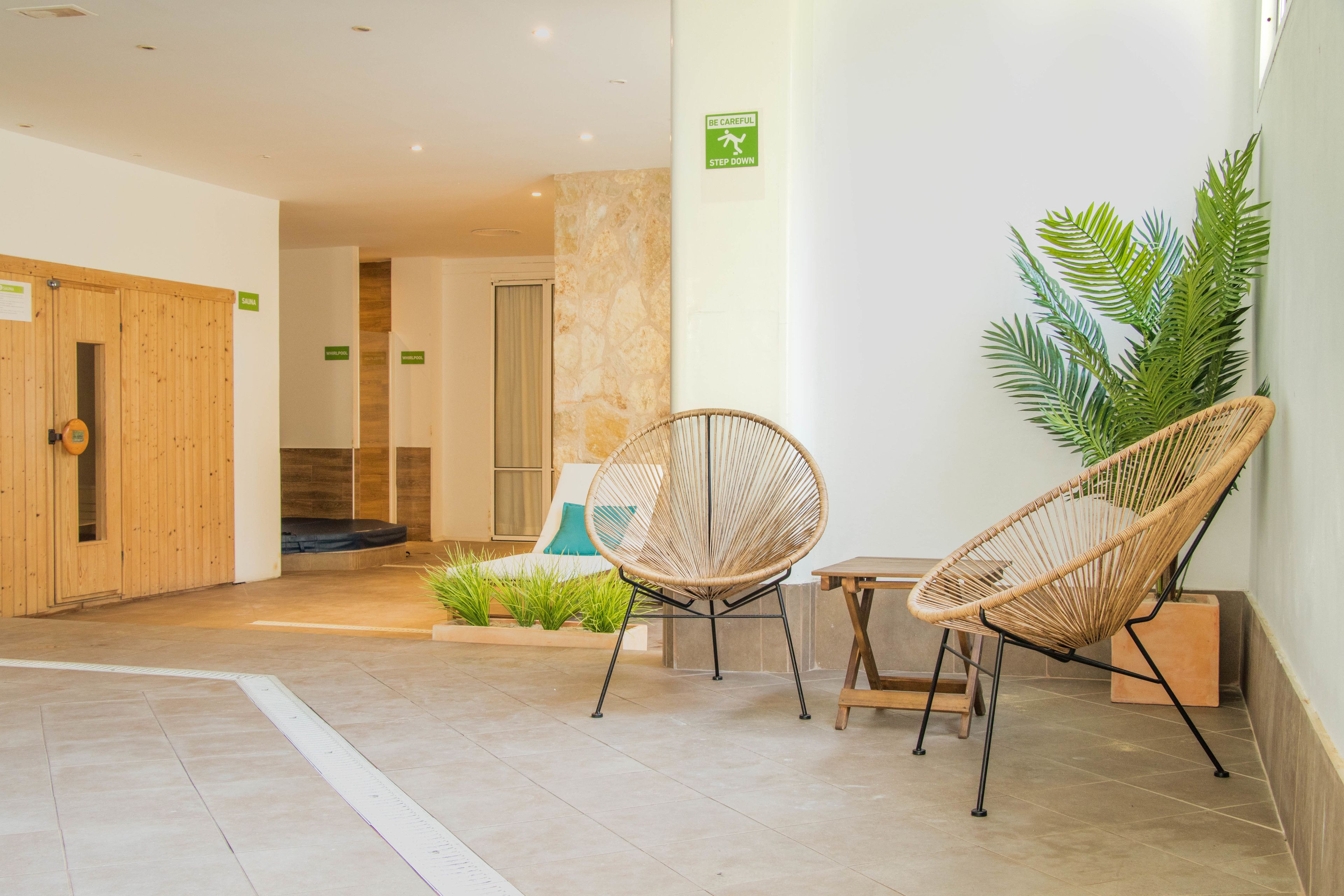 Un hall d’entrée avec une porte en bois, un comptoir d’accueil, deux fauteuils en osier, une petite table et une plante en pot.