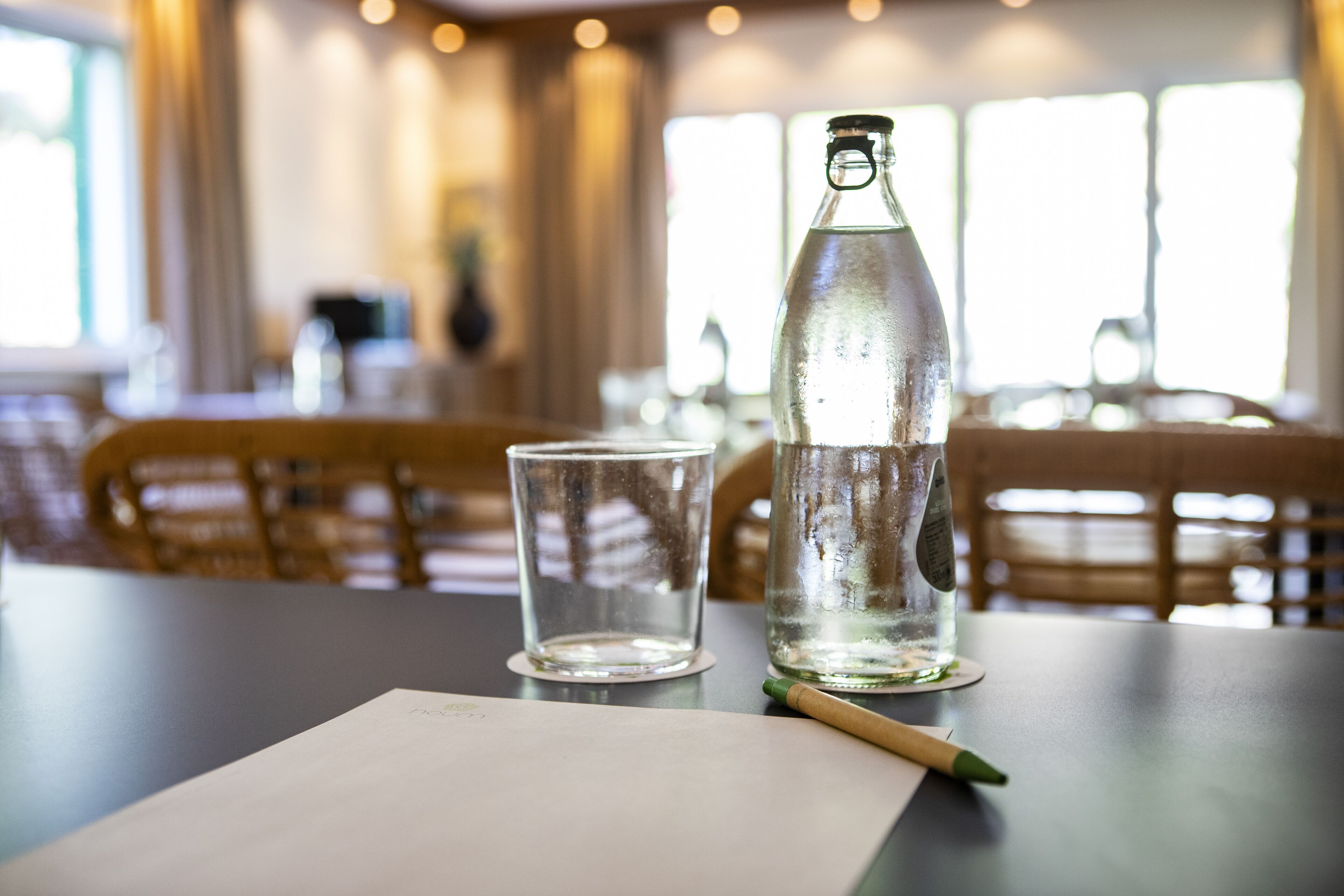 A bottle of water and a glass on a table in a restaurant setting.